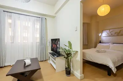 a bedroom with a bed and a table and a window at Forbeswood Heights 1Br with Garden view in Manila