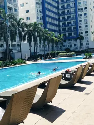a pool with chairs and palm trees and buildings at Ederly Place at Sea Residences near Moa in Manila