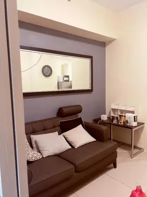 a living room with a brown couch and a mirror at Jazz Residences Tower B Makati in Manila