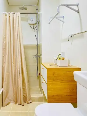 a bathroom with a shower curtain and a wooden dresser at Staycation by Mailine in Manila