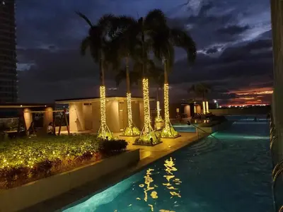 a swimming pool at night with palm trees and lights at La Luz 0835 Smdc Breeze in Manila