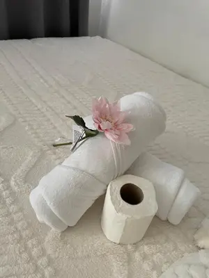 a roll of toilet paper and a flower on a bed at 12 Minutes from Mall of Asia - Spacious Condo with Balcony & Hot Shower in Manila