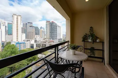 a balcony with a table and chairs and a view of the city at Greenbelt Makati Condo with Balcony & Park Views in Manila