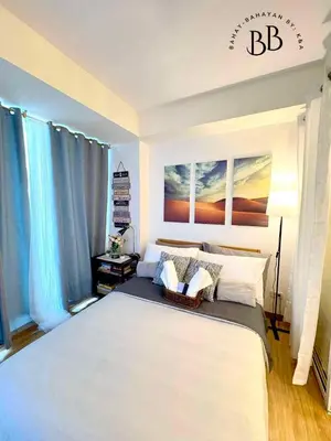 a bedroom with a large white bed with blue curtains at Bahay-Bahayan by K&A at Azure Urban Resort Residences in Manila