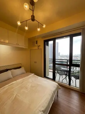 a bedroom with a bed and a balcony with a table at Grand Soho Makati Condo in Manila