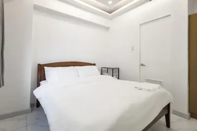 a white bed in a white room with a ceiling at Central BGC Forbeswood Heights in Manila