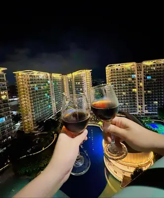 two people holding glasses of wine in front of a city at Azure Resort Residence, 1bedroom with balcony Beach view in Manila