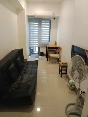 a living room with a black couch and a fan at FAME Bedroom in Manila