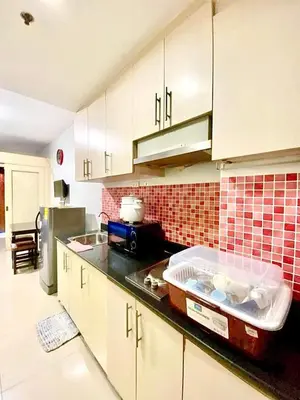 a kitchen with white cabinets and a red tiled wall at Sea residences by mavis in Manila
