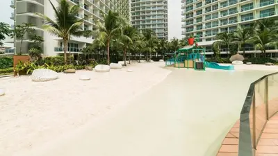 a beach at the resort with palm trees and buildings at Cozy Apartment Azure Urban Resort Residences in Manila