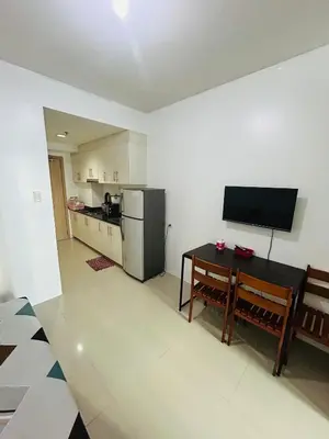 a kitchen with a refrigerator and a table and a television at Sojourn at Sea Residences MOA in Manila
