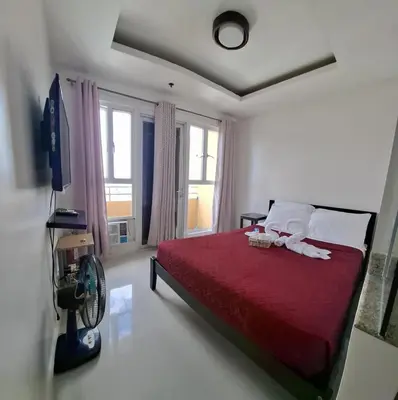 a bedroom with a red bed and a tv and windows at Modern Studio Birch Tower Near Malls & Nightlife in Manila