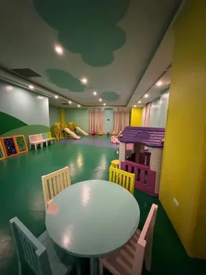 a room with a table and chairs and a playroom with a table and people at Industrial Chic Studio in McKinley Hill Walk to Venice Mall in Manila