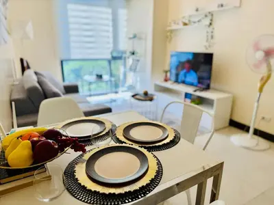 a table with plates and a bowl of fruit on it at Cozy Viceroy 1BR, Walk to Venice Mall in Manila