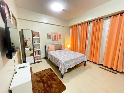 a bedroom with a bed and a tv and orange curtains at Airport NAIA T3 Condotel in Manila