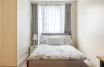 a small bedroom with a bed and a window at BGC Taguig Uptown 3BR corner unit with pool view, bath tub, wifi, parking, beside Landers BGC in Manila