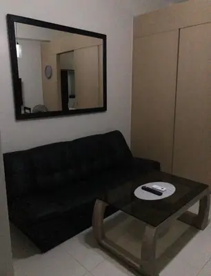 a living room with a black couch and a mirror at Field Residence Staycation in Manila