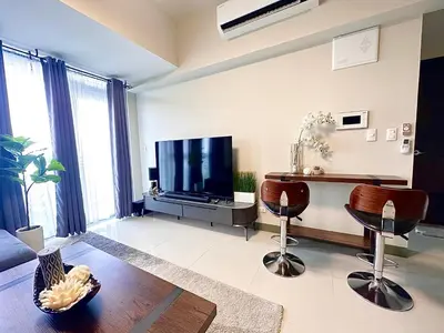 a living room with a flat screen tv and two chairs at City Lights Apartment in BGC in Manila