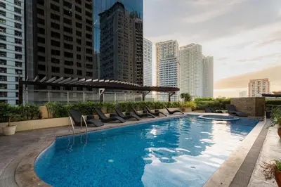 a large swimming pool with chairs and buildings at Studio Penthouse in Greenbelt - Park View & Pool in Manila