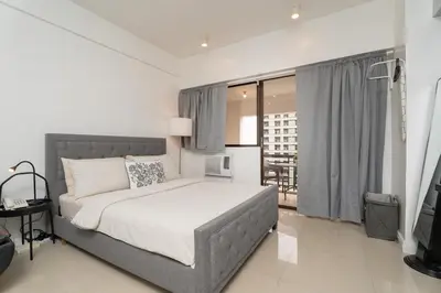 a bedroom with a large bed and a balcony at Charming Greenbelt Condo with Balcony & Pool Access in Manila