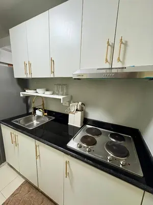 a kitchen with a stove and a sink and white cabinets at Comfy Cozy Staycation in Manila