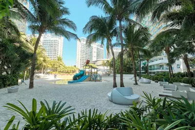 a beach with a playground and palm trees and buildings at Bahamas Tower Azure Urban Resort Residences by Nestled Nook in Manila