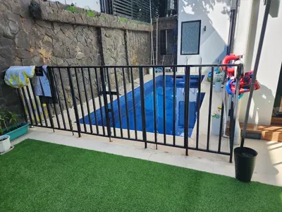 a black fence with grass next to a swimming pool at Family room with private pool in Manila