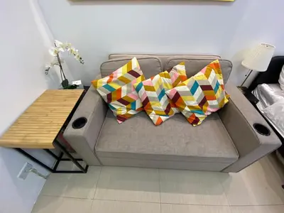 a couch with two pillows and a wooden table at The Grand Staycation at MOA - Unit 7102 Hotel-like in Manila