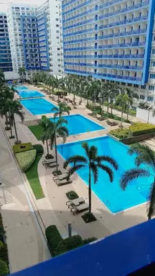 a group of pools with palm trees and a large building at Sea Residences Mall of Asia- Jerson in Manila