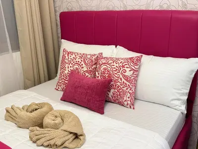 a bed with a pink headboard with pillows and towels at Shore Residences Sunset Room facing Manila Bay & City View RM1641 by Prime Stay MOA in Manila