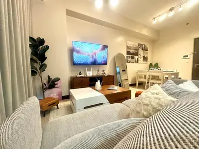 a living room with a couch and a tv on the wall at Cozy 1BR at Greenbelt Hamilton Makati in Manila
