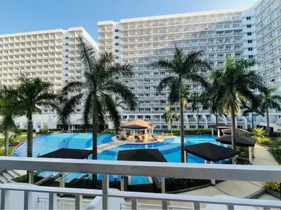 a swimming pool with palm trees in front of a large building at Shell Residences - Rhoi in Manila