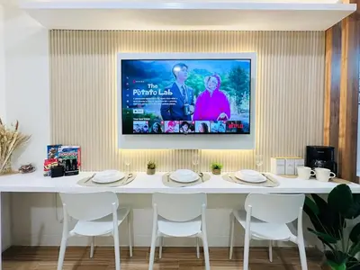 a tv hanging on a wall above a table with white chairs at Getaway Haven at Southwoods, Biñan with Fast Internet in Biñan