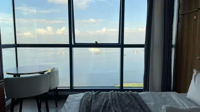 a bedroom with a bed and a table and a large window at 3BR Grand Riviera Suites by MrSayla in Manila