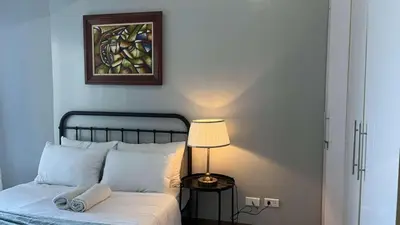 a bed with a lamp and a painting on the wall at 3BR Grand Riviera Suites by MrSayla in Manila