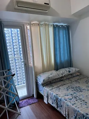 a bedroom with a bed with blue curtains and a window at Studio Units at SM Light Residences Condo Beside Boni MRT Station in Manila