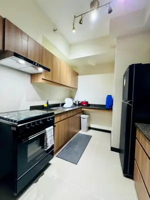 a kitchen with black appliances and wooden cabinets at Metro Zen at DMCI Satori Residence 1br in Manila