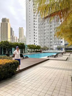 a woman standing next to a swimming pool in a city at The Essential 2 BR at Sm Jazz makati 100 mbps in Manila
