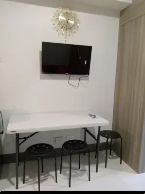 a white table with four chairs and a tv on a wall at One Bedroom Unit in Fame Residences in Manila