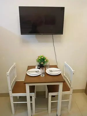 a wooden table with two chairs and a television on a wall at la Chicka - 295 T3 in Manila