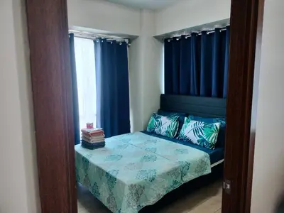 a bedroom with a bed with blue curtains and a mirror at 1 Bedroom Near Airport by Rqui in Manila