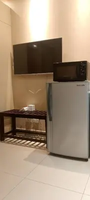 a tv on a wall with a table and a refrigerator at Shell Residence in Manila