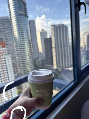 a person holding a cup of coffee in front of a window at Skyline Blue Air residences 1Br cityview by Tin & Aix in Manila
