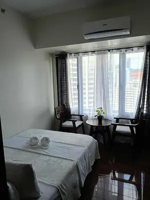 a bedroom with a bed and a table and a window at Skyline Blue Air residences 1Br cityview by Tin & Aix in Manila