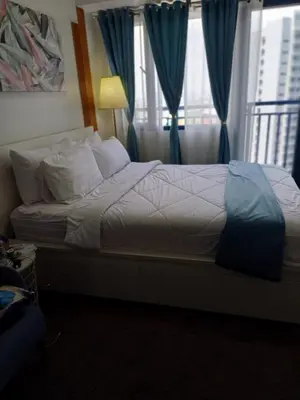 a bedroom with a bed with blue curtains at Cozy Suites in Air residence in Manila