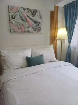 a bedroom with a white bed with a painting on the wall at Cozy Suites in Air residence in Manila