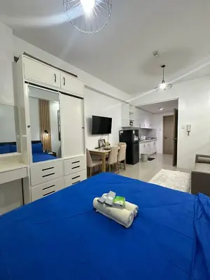 a bedroom with a blue bed and a living room at Shore Residences Mall of Asia in Manila