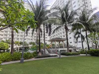 a park in front of a large building with palm trees at La Vie Riche Holiday Homes - Cozy 1BR Apartment near MOA in Manila