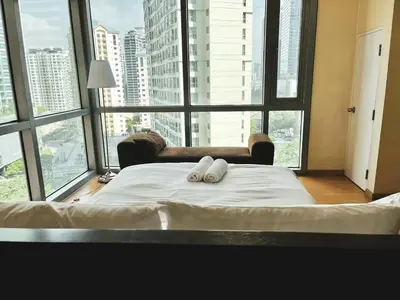 a bed with two towels on it in a room with large windows at Budget City View w Pool Access in BGC Taguig City in Manila