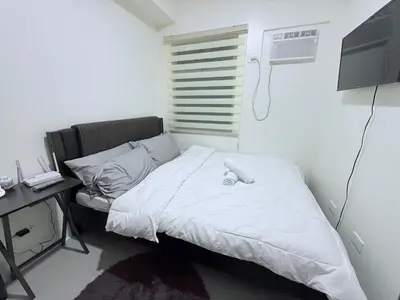 a white bed in a room with a desk and a window at Urban Deca Towers Cubao in Manila